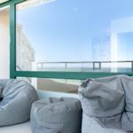 Große Fenster mit Blick auf den Strand. Graue Sitzkissen und ein kleiner Tisch.