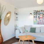 Wohnzimmer mit Sofa, Tisch und Wandbild. Großer Vasen mit Pflanze und Dekoration.
