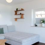 Ein Raum mit Sofa, Wandregal und Fenster mit Blumen.