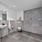 Badezimmer mit Dusche, Waschbecken und Toilette. Graue Fliesen und Spiegelschrank.
