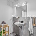 Badezimmer mit Waschbecken, Spiegel, Handtuch und Pflanze auf Holzregal.