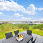 Terrasse mit Tisch und Stühlen, Blick auf Hafen mit Booten und Gras.