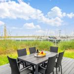 Terrasse mit Tisch und Stühlen, Blick auf Hafen mit Booten und Gras.