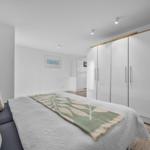 Schlafzimmer mit Bett, Kleiderschrank und Wohnbereich im Hintergrund.