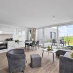 Wohnküche mit Essbereich und Terrasse. Modern eingerichtet mit grauer Couch und Sitzgruppe.