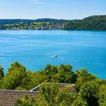 Weitläufiger Blick auf einen See mit Boot und grünen Hügeln im Hintergrund.