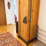Holzschrank mit Metallbeschlägen, Teppich und Kleiderständer im Raum.