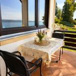 Terrasse mit Tisch, Stühlen und Blick auf See und Garten.