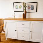 Weißer Sideboard mit Holzoberfläche, zwei Bilder und Dekoration.