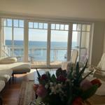 Wohnzimmer mit Meerblick durch große Fenster und Balkon mit Sitzgelegenheiten.
