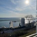 Blick auf Hafen mit Schiffen und Leuchtturm unter blauem Himmel.