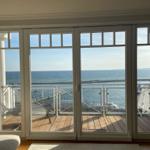 Durch große Fenster blickt man auf einen Hafen mit Booten und das Meer.