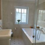 Badezimmer mit Badewanne, Dusche und Waschbecken. Fenster mit Blumen.