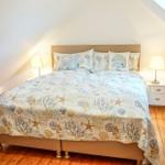Schlafzimmer mit Bett, Nachttisch und Dachschrägen. Holzboden und Fenster.