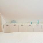 Schlafzimmer mit Dachschrägen, Bett und weißen Schränken mit Dekoration.