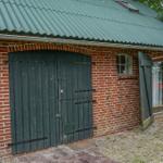 Rotes Backsteinhaus mit grünem Dach, Holztür und Fenster mit Vorhängen.
