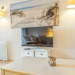Wohnzimmer mit Fernseher, Wandbild und Tisch. Vorhänge und Heizkörper sind sichtbar.