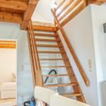 Holztreppe führt zur oberen Etage. Im Vordergrund steht ein Kaminofen.