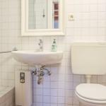 Badezimmer mit Dusche, Waschbecken und Toilette. Weiße Fliesen und Spiegel.