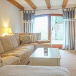 Wohnzimmer mit Sofa, Couchtisch und TV. Holzbalken an der Decke und Fenster mit Vorhängen.