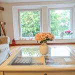 Wohnzimmer mit Sofa, Glas-Tisch und Blick auf grüne Bäume durch Fenster.