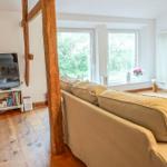 Wohnzimmer mit Sofa, Fernseher und Holzbalken. Große Fenster mit Blick auf Grün.