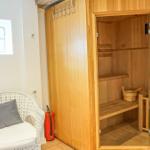 Sauna mit Holzbank und Eimer. Weiße Stuhllehne mit Kissen. Fenster mit Gitter.