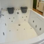 Eine große weiße Whirlpool-Badewanne mit Armlehnen und mehreren Düsen.