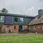 Haus mit Strohdach und Backsteinfassade, Gartenbereich mit Tisch und Stühlen.