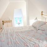 Schlafzimmer mit Dachschrägen, Bett mit Blumenbezug und kleinem Fenster.