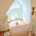 Schlafzimmer mit Bett, Holzboden und Fenster. Weiße Wand und goldener Bettkopf.