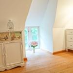 Schlafzimmer mit Holzboden, weißen Schränken und Dachfenster. Auf einem Schrank stehen Wecker und Lampe.