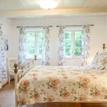 Schlafzimmer mit Bett, Fenstern und floralen Vorhängen.