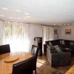 Wohn- und Essbereich mit Sofa, Esstisch und Kaminofen. Fenster mit weißen Vorhängen.