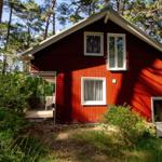 Rotes Holzhaus mit weißen Fenstern im Wald. Terrasse mit Sitzgelegenheit.