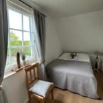 Schlafzimmer mit Bett, Stuhl und Fenster mit Blick auf Grün.
