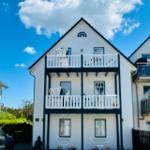 Weiße Hausfassade mit drei Balkonen und Fenstern unter blauem Himmel.