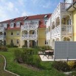 Gelbes Mehrfamilienhaus mit weißen Balkonen und rotem Dach. Gartenbereich mit Tisch und Stühlen.