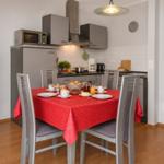 Küche mit Esstisch, roter Tischdecke und vier Stühlen. Hintergrund: Küchenschränke und Küchenzeile.