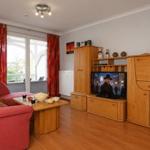 Ein Wohnzimmer mit rotem Sofa, Holzmöbeln und Fernseher. Durchgang zur Terrasse mit roten Vorhängen.