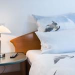 A bed with pillows and bedding featuring seagull patterns. Nightstand with lamp and remote control.