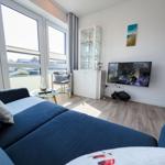 A living room with a blue sofa, large windows, and a TV mounted on the wall.