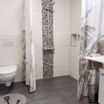 Bathroom with shower, toilet, and sink. Tiles and shower curtain with pattern.
