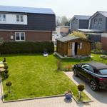 Backyard with garden, wooden shed, and paved parking area with car.