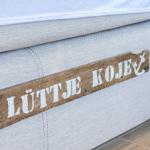 Ein Bett mit einem Holzschild, das LÜTTE KOJE schreibt.