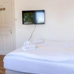 Schlafzimmer mit weißem Bett, Fernseher an der Wand und Tür zum Bad.