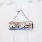 Holz-Hakenplatte mit blau-weißem Seil hängt an einer weißen Tür.