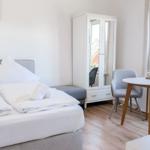 Schlafzimmer mit Bett, Kleiderschrank und Tisch. Fensterblick auf Dach und Garten.