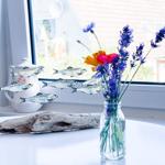 Auf dem Tisch steht eine Vase mit Blumen und ein Fischschwarm-Objekt neben einem Holzstück.