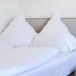 Ein Bett mit weißer Bettwäsche und zwei Kissen. An der Wand ist ein grauer Kopfteil.